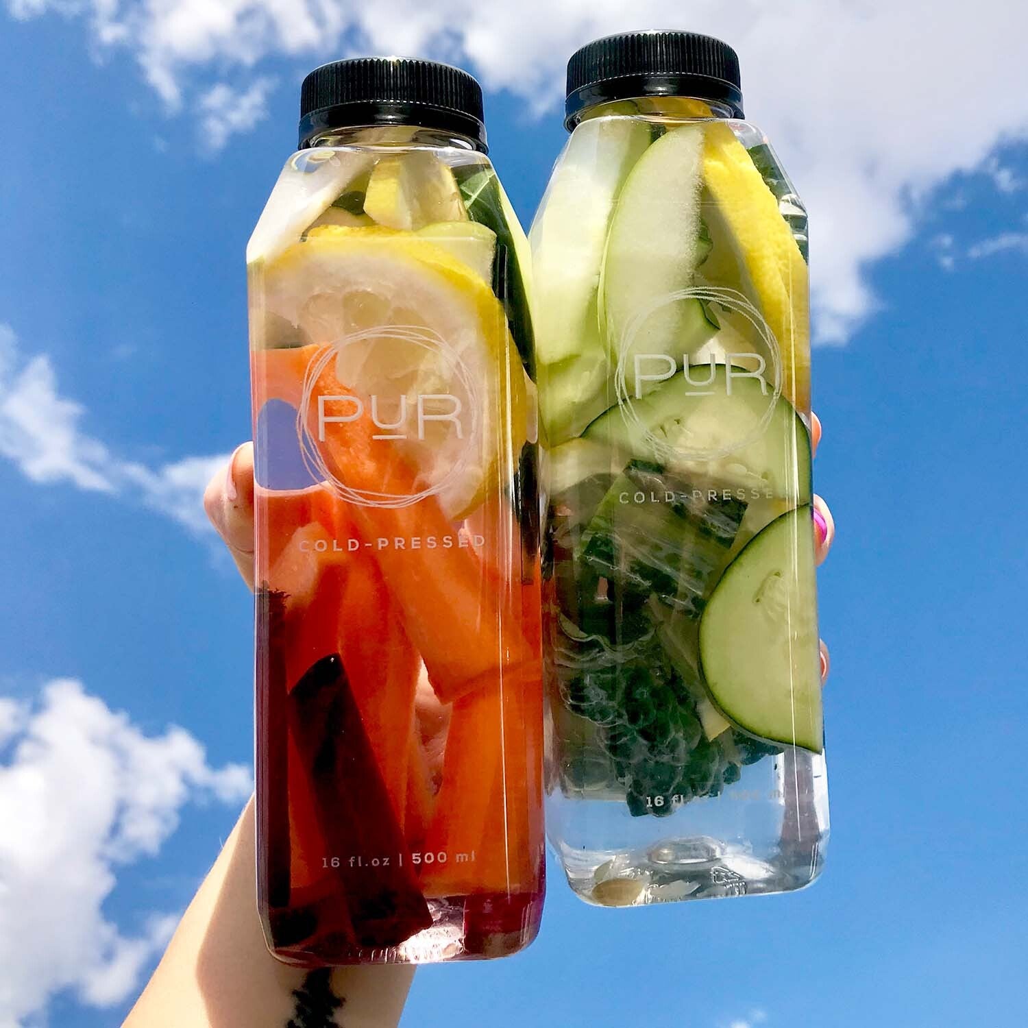 hand holding 2 bottles of fresh fruit and vegetables in front of a blue sky